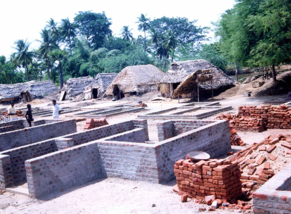 1992: In Canoor (Indien) bauen wir 25 Backsteinhäuschen. Im Hintergrund die alten Lehmhütten mit ihren wasserdurchlässigen  Strohdächern